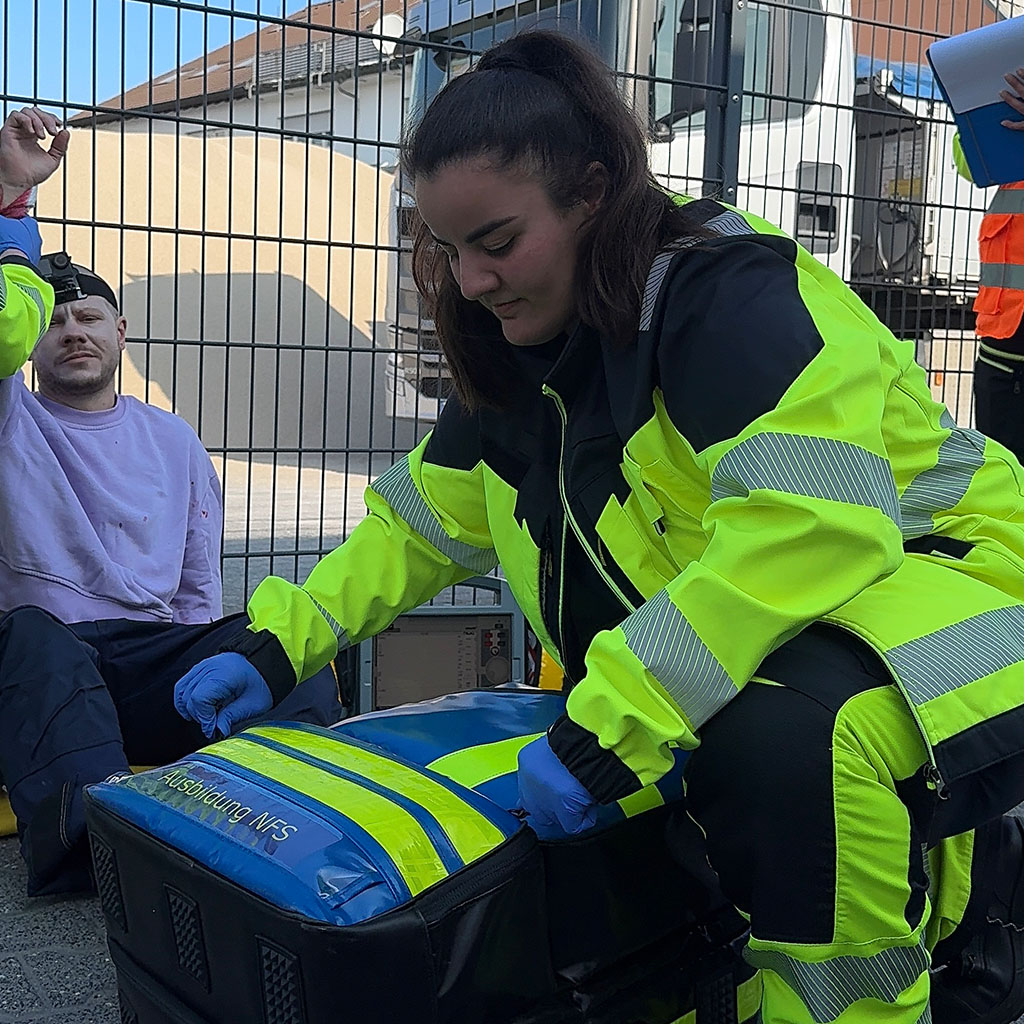Auszubildende zur Notfallsanitäterin öffnet bei einer Übung den Notfallrucksack